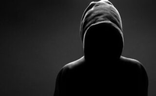 Dark image of a person with a hood on and no face: Satan uses deception