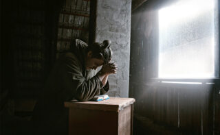 Man praying in dark room with window light beside him